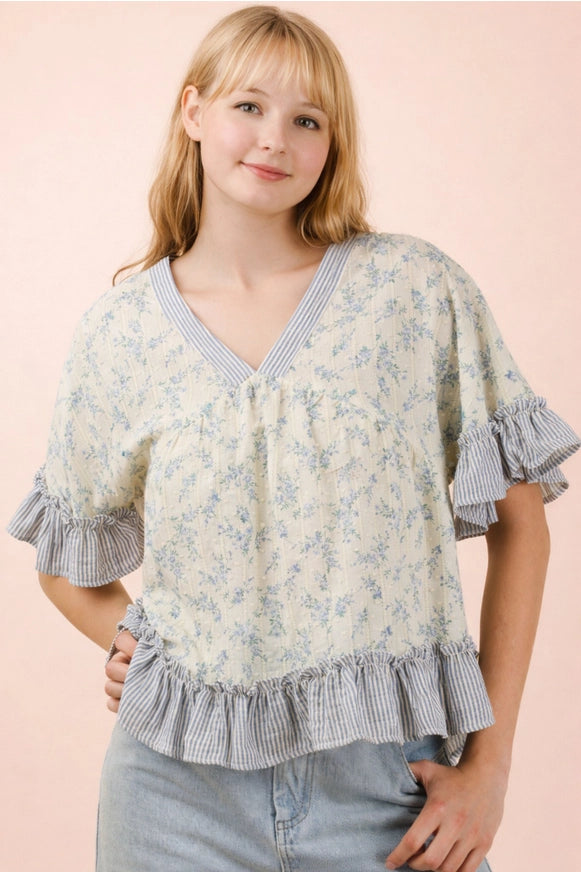 Woman wearing a floral blouse with ruffled sleeves and hem on a pink background