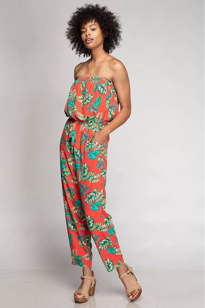 Woman wearing a strapless jumpsuit with a tropical leaf pattern on a plain background
