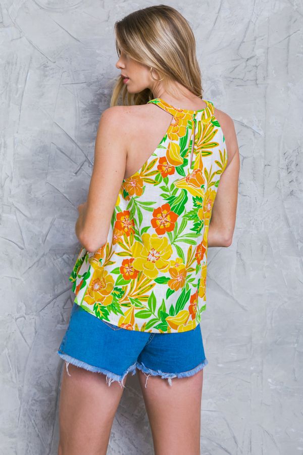 Woman wearing a colorful floral top and blue shorts against a gray textured wall.