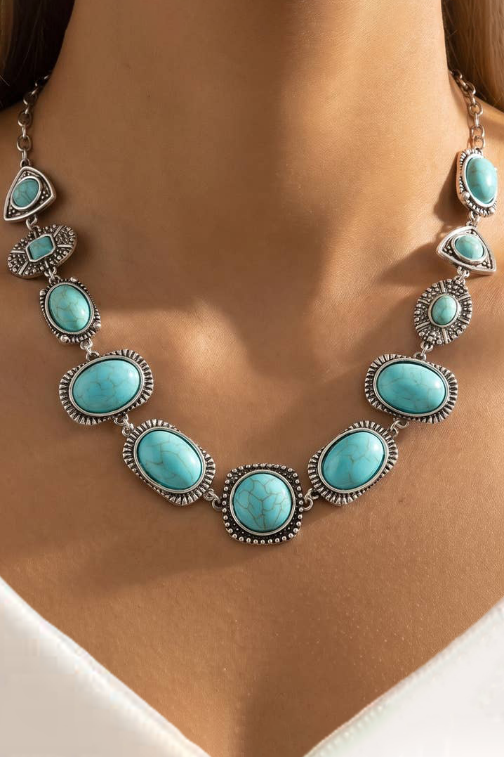 A close-up of a woman's neck wearing a silver-toned statement necklace with multiple oval turquoise-blue stones in ornate bezel settings.