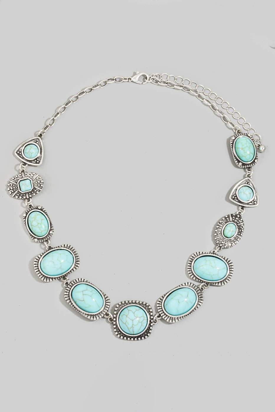 A silver-toned statement necklace featuring multiple oval and triangular turquoise-colored stones set in textured silver bezels, displayed on a neutral light gray background.