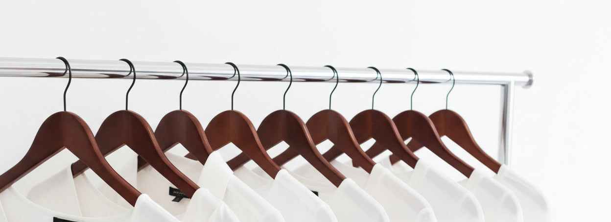 Row of white shirts on wooden hangers against a white background